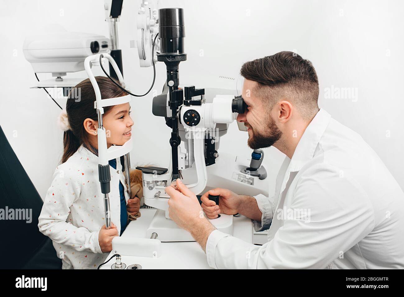 L'ophtalmologiste mâle vérifie la vue d'une petite fille avec un équipement ophtalmique spécial. GRL sourit parce que sa vue est très bonne Banque D'Images
