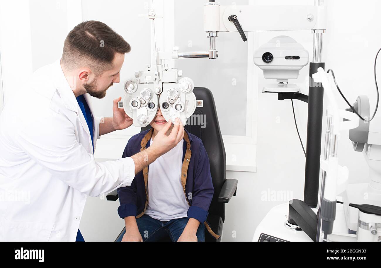 Optométriste homme vérifiant la santé oculaire et l'acuité visuelle des adolescents. Phoropter - un dispositif de mesure de l'erreur de réfraction et de détermination de l'information Banque D'Images