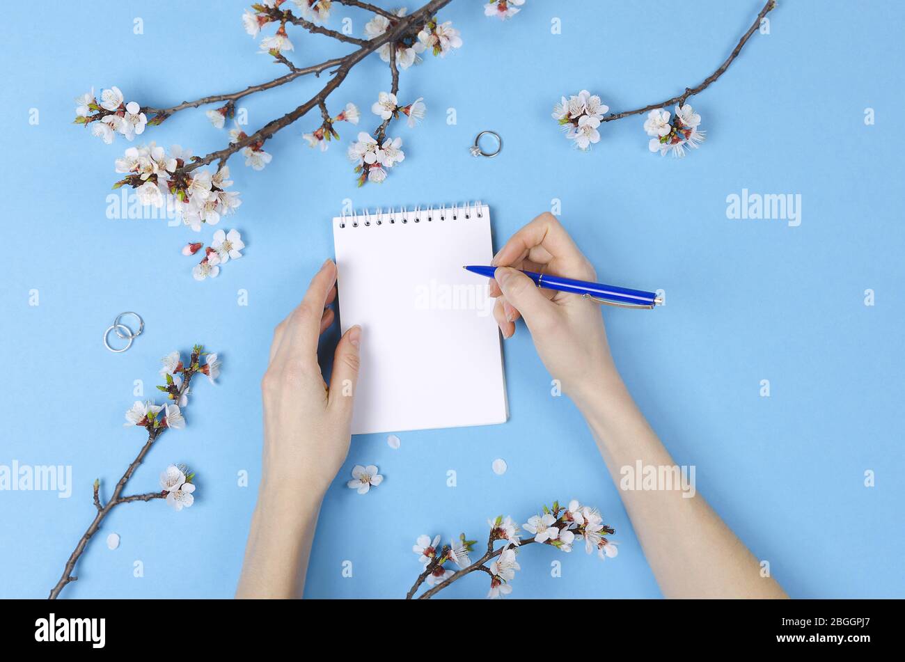 Fille écrivant la liste de souhaits pour les plans futurs. composition de plat avec fleurs, bloc-notes. Planification de mariage Banque D'Images
