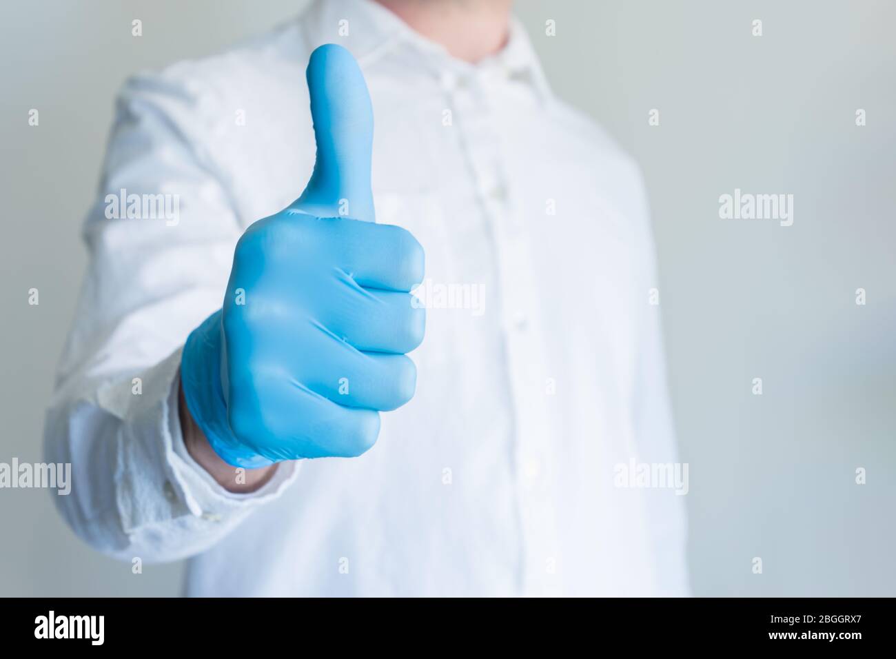Homme dans un gant médical bleu montrant l'approbation pouces vers le haut s'inscrire sur fond blanc avec espace de copie pour le texte. Banque D'Images
