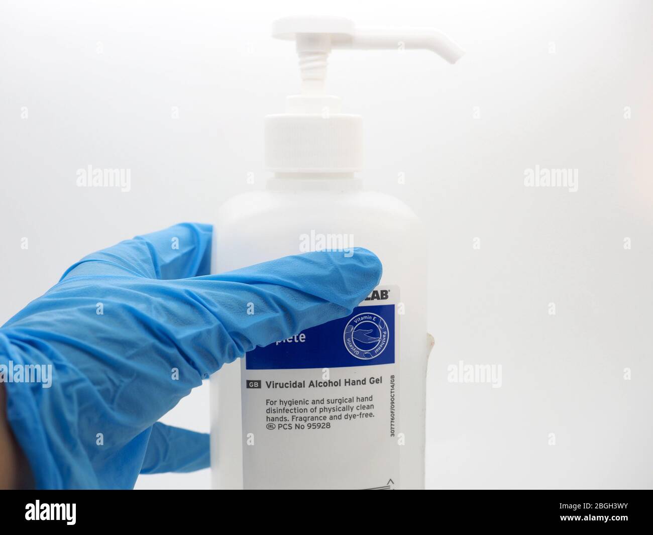 Une main, portant UN gant bleu jetable ramasser UNE bouteille de gel aseptisant, Londres, Royaume-Uni Banque D'Images