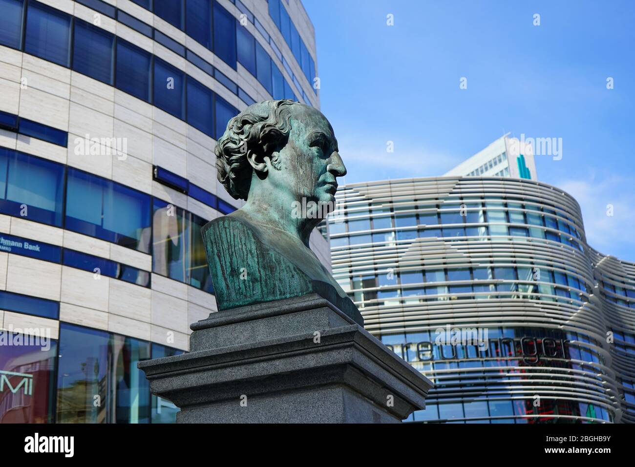Ancienne et nouvelle : sculpture en bronze historique de Friedrich Wilhelm von Schadow (peintre allemand), inaugurée en 1869, devant un complexe de bureaux/magasins moderne. Banque D'Images