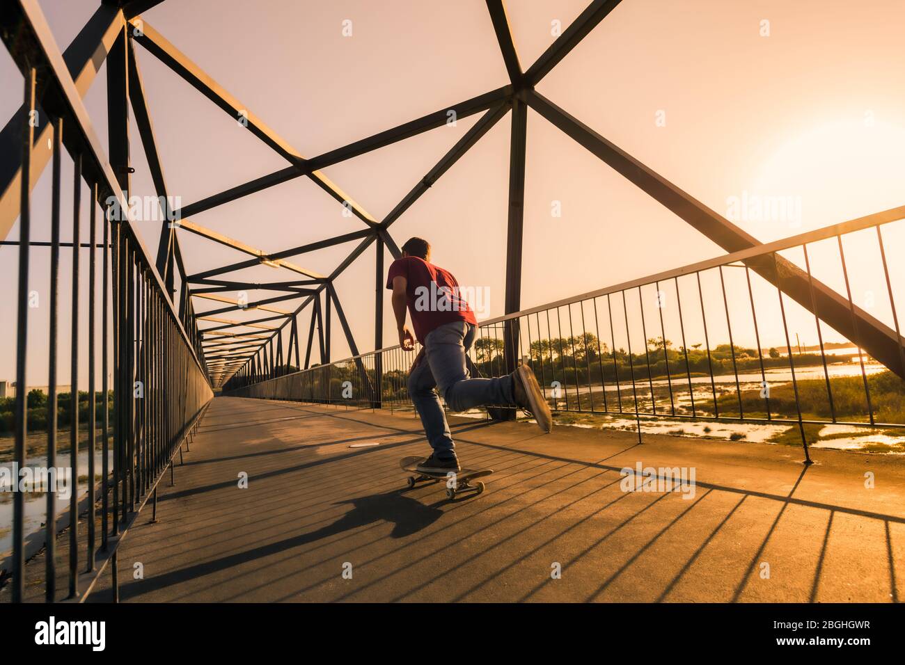 La vitesse du skate-boarder passe par le pont piétonnier au coucher du soleil. Banque D'Images