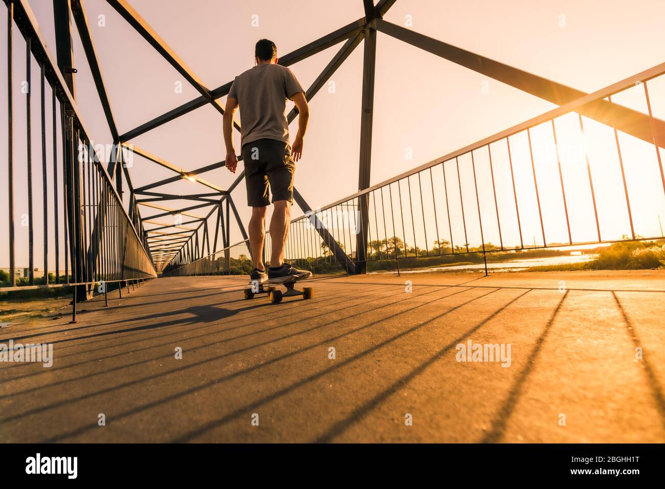 La vitesse du skate-boarder passe par le pont piétonnier au coucher du soleil. Banque D'Images