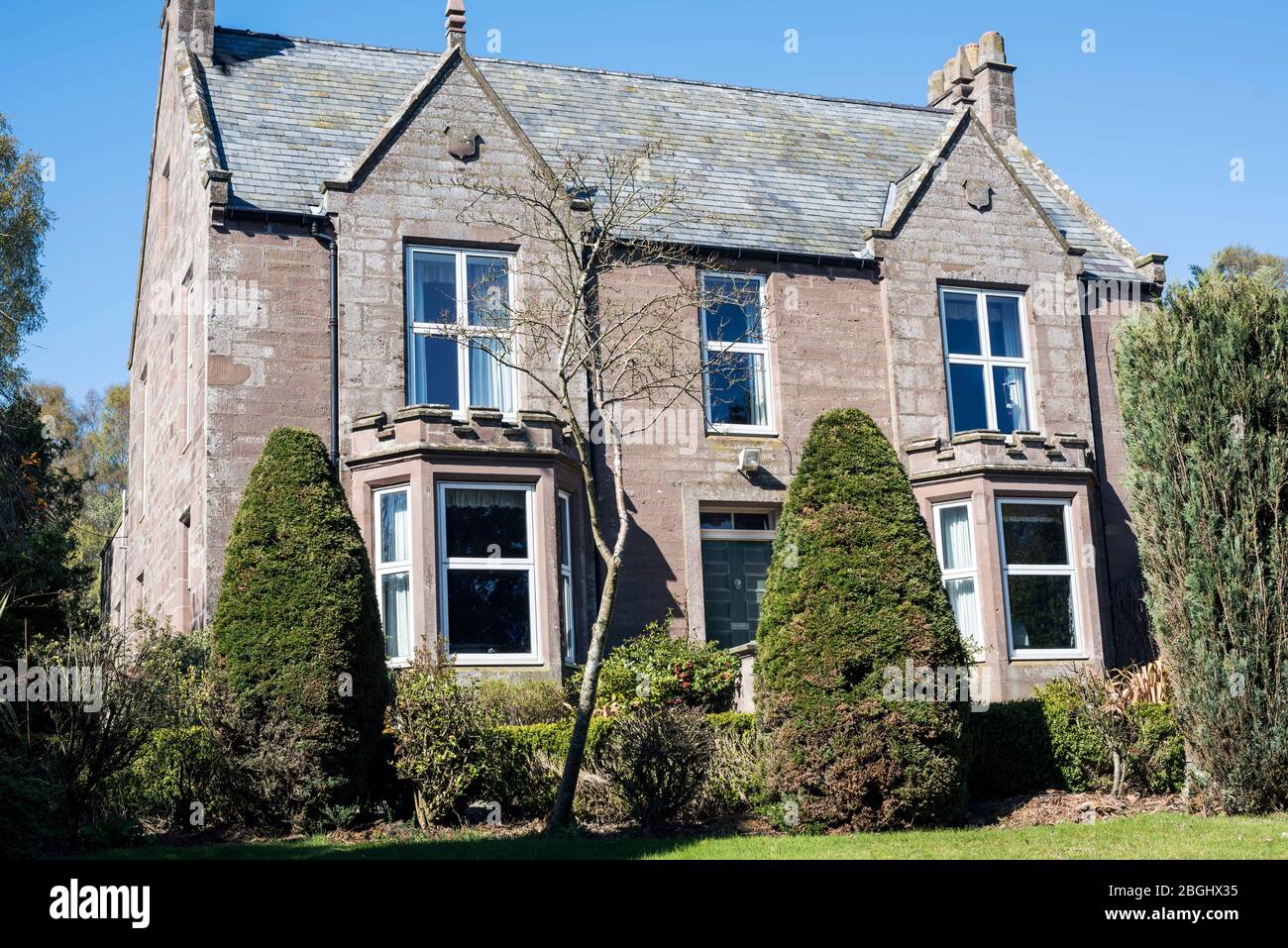 Grande ancienne maison victorienne en grès écossaise construite en 1852 avec de vieux arbustes et de petits arbres en premier plan, contre un ciel bleu. Banque D'Images