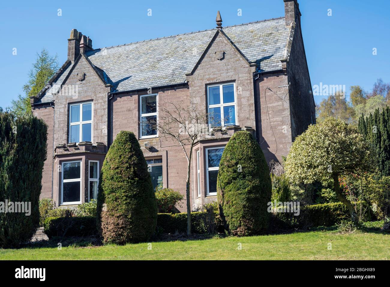 Grande ancienne maison victorienne en grès écossaise construite en 1852 avec de vieux arbustes et de petits arbres en premier plan, contre un ciel bleu. Banque D'Images