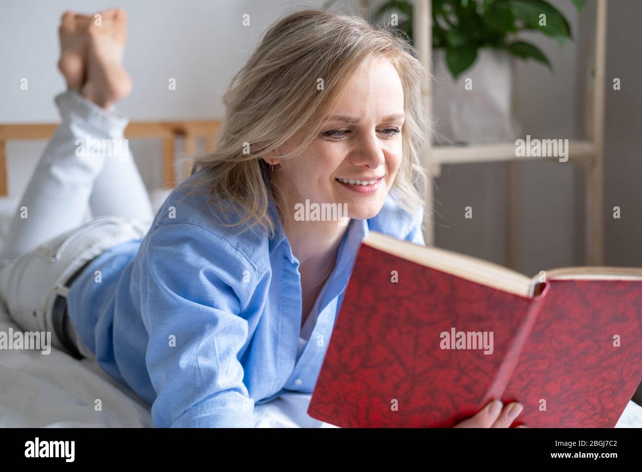 blonde femme tenant livre ouvert et lecture couché sur le lit. Loisirs, rester à la maison et quarantaine. Le temps pour vous Banque D'Images