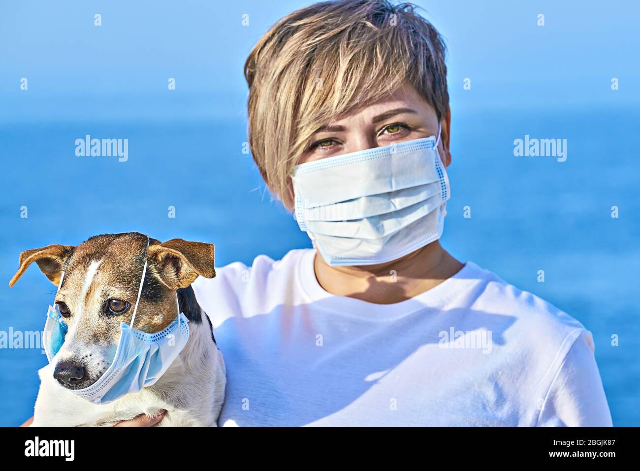 La femme présente un masque protecteur maintient le chien portant un masque médical. La maladie du coronavirus COVID-19 est dangereuse pour le concept d'animaux de compagnie Banque D'Images