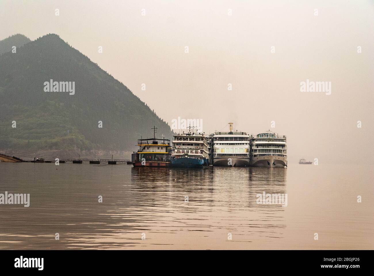 Fengdu, Chine - 8 mai 2010: Coup de matin sur l'eau brune Yangtze River sous brouillard et ciel smog sur 4 bateaux de passagers amarrés au pont ponton de termina Banque D'Images