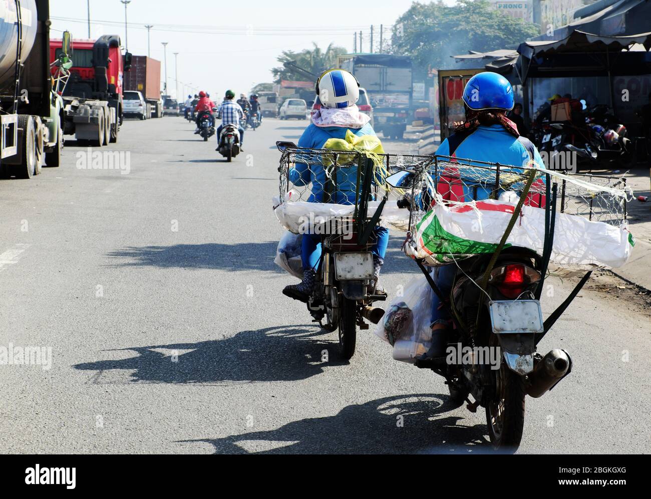 Derrière vue deux vietnamiennes tour moto transport panier vide après avoir vendu la nourriture à midi, ombre réfléchir sur la surface de la route, Ho chi Minh ville Banque D'Images