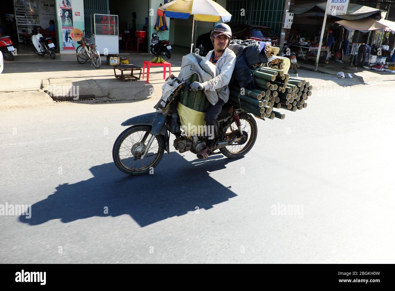 DONG NAI, VIET NAM, homme vietnamien à moto sur la route et le transport morceau de tronc de bambou, son ombre réfléchit sur la surface de la route, Vietnam Banque D'Images