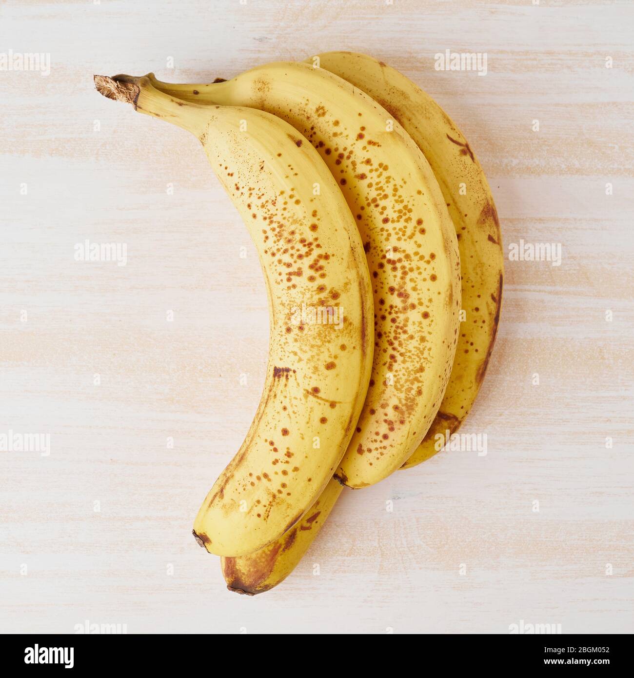 Bananes mûres avec taches brunes sur table en bois blanc vif Banque D'Images