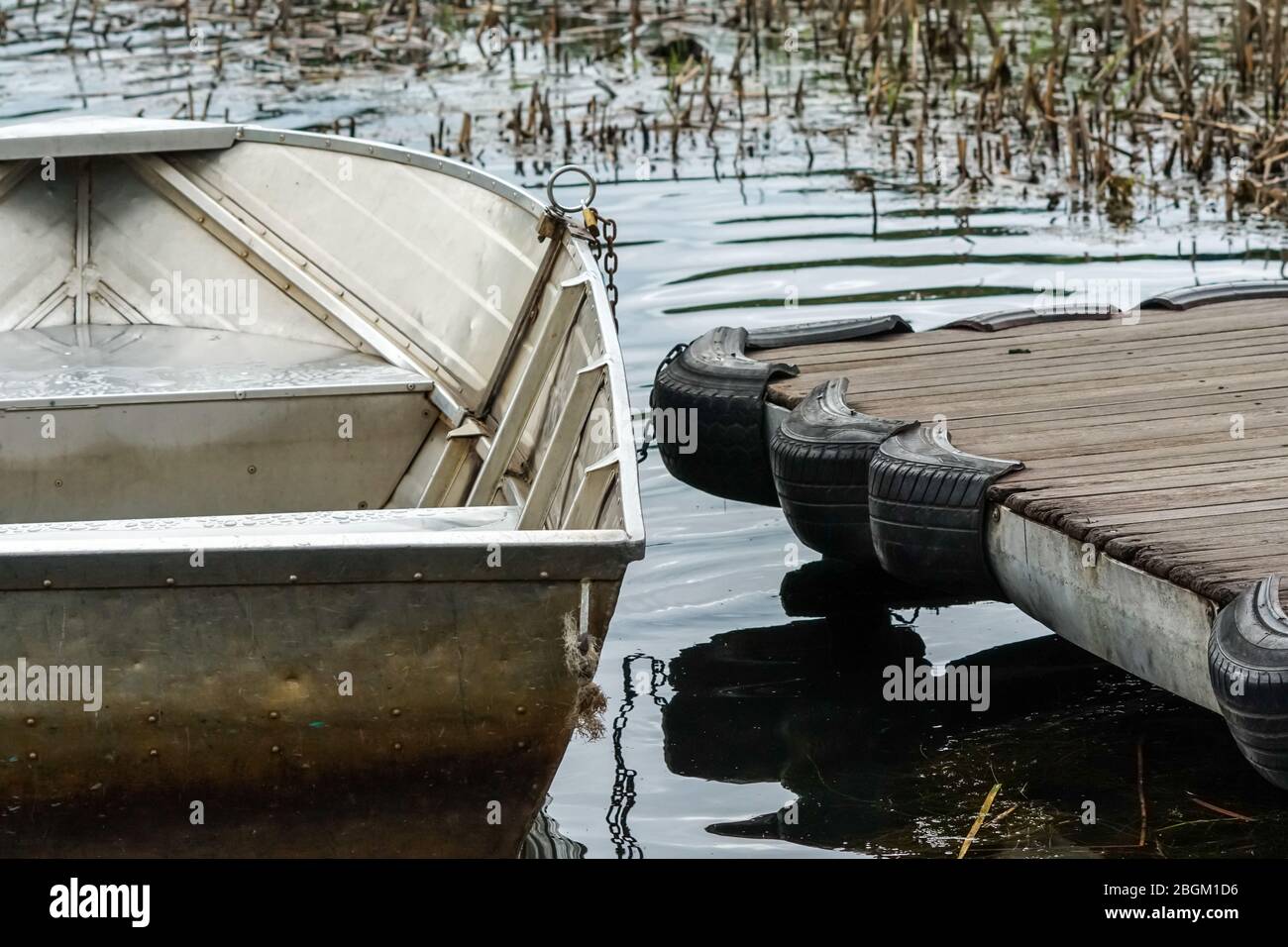 Bateau à rames d'aluminium amarré à une jetée en bois sur un lac avec des ondulations dans l'eau et roseaux dans le concept de fond abstrait plaisir et loisirs d'été Banque D'Images