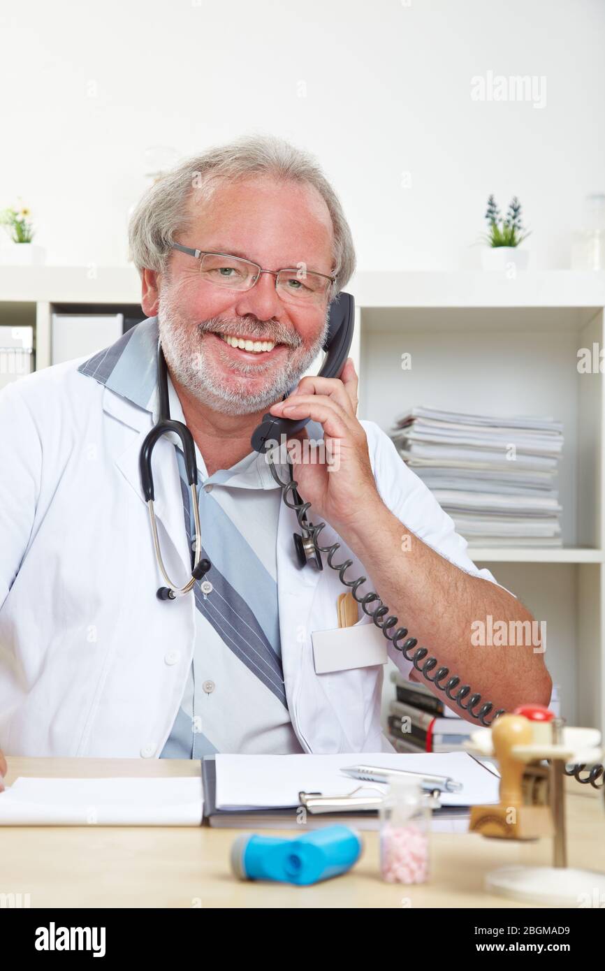 Médecin souriant assis au téléphone dans sa pratique Banque D'Images
