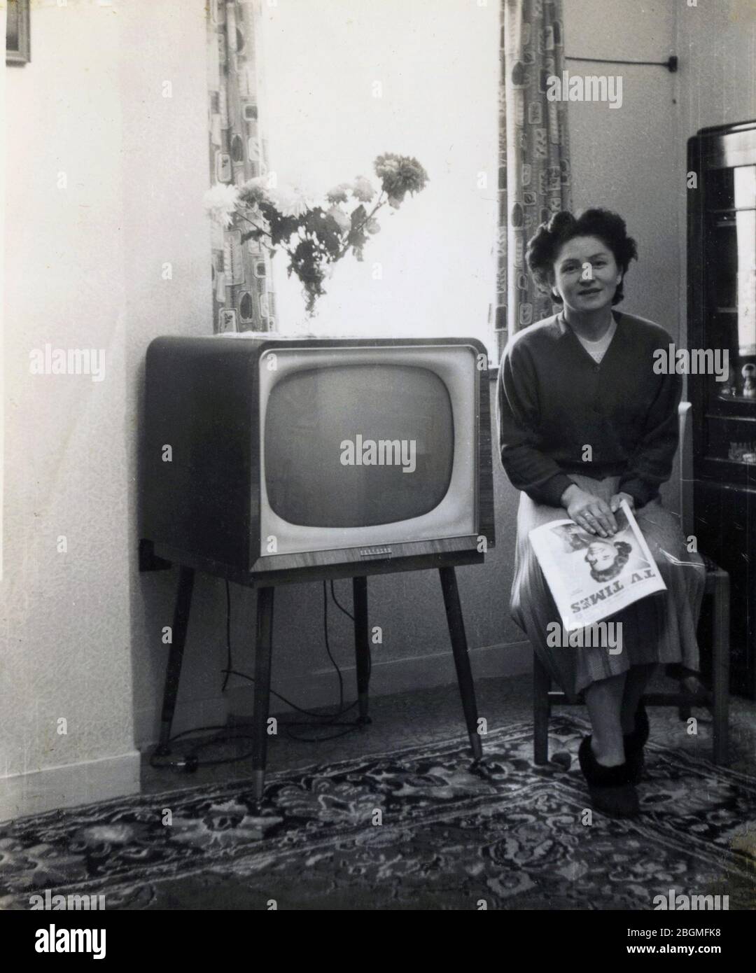 1958, historique, à l'intérieur d'une pièce, une dame assise pour une photo à côté de son téléviseur de l'époque, tenant une copie du magazine de liste de télévision, TV Times, Angleterre, Royaume-Uni. Publié pour la première fois en 1955, le magazine était la seule source d'information sur la programmation sur ITV, lancé la même année, comme un réseau de télévision alternatif au radiodiffuseur public BBC Television, qui avait été créé en 1936. Banque D'Images