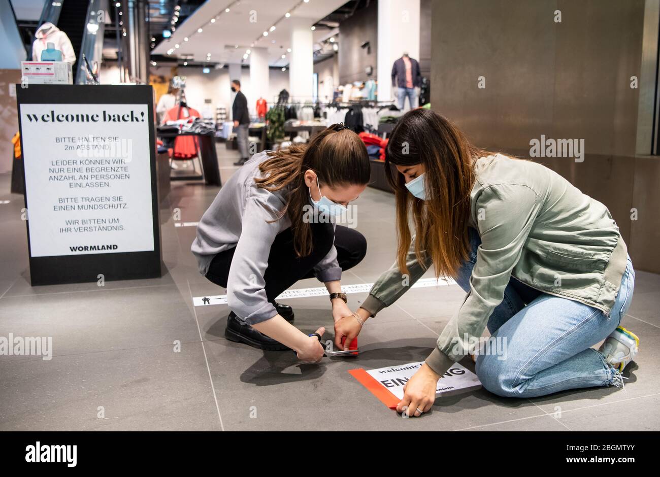 22 avril 2020, Berlin: Les employés d'un magasin de vêtements du Mall of Berlin, qui portent des protecteurs de bouche et de nez en raison de la pandémie de Corona, collez un panneau sur le sol avec les mots "entrée". Le magasin a réduit sa zone de vente à moins de 800 mètres carrés et ne permet qu'à un nombre limité de clients d'entrer par l'entrée unique. À partir d'aujourd'hui, Berliners peut encore une fois faire des achats dans de nombreux magasins au-delà du commerce alimentaire. Les détaillants ayant une zone de vente de 800 mètres carrés peuvent rouvrir après une décision du Sénat. L'accès au magasin doit être contrôlé - un seul client pour 20 mètres carrés i Banque D'Images