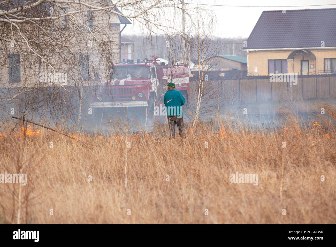 l'homme met le feu sur l'herbe brûlante. L'herbe brûle dans la prairie près d'un bâtiment résidentiel privé. Azov district national allemand de la région d'Omsk, Russie Banque D'Images