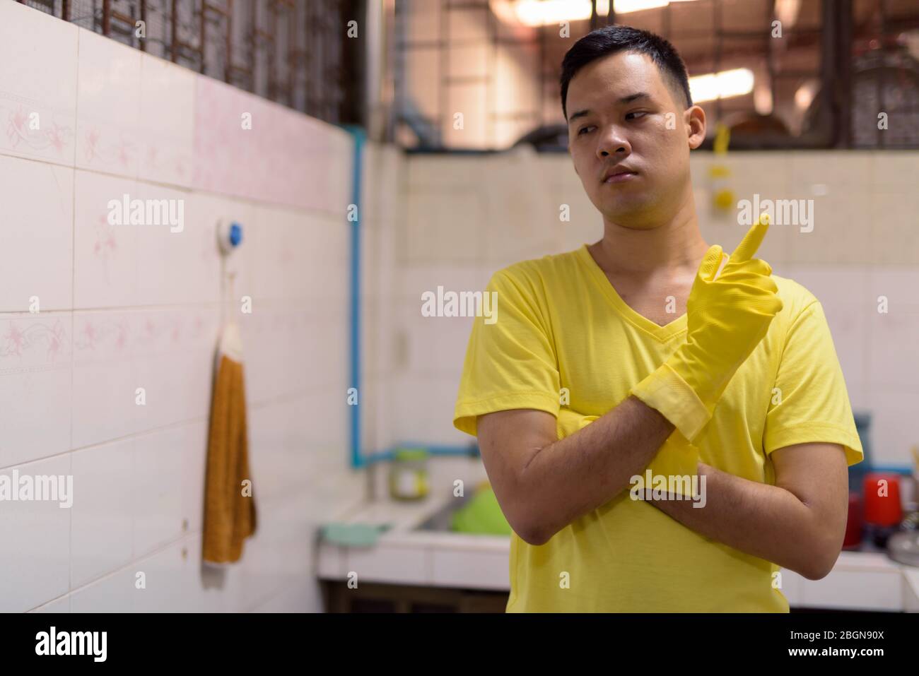 Jeune homme asiatique avec des gants de pensée et de faire des corvées de maison Banque D'Images