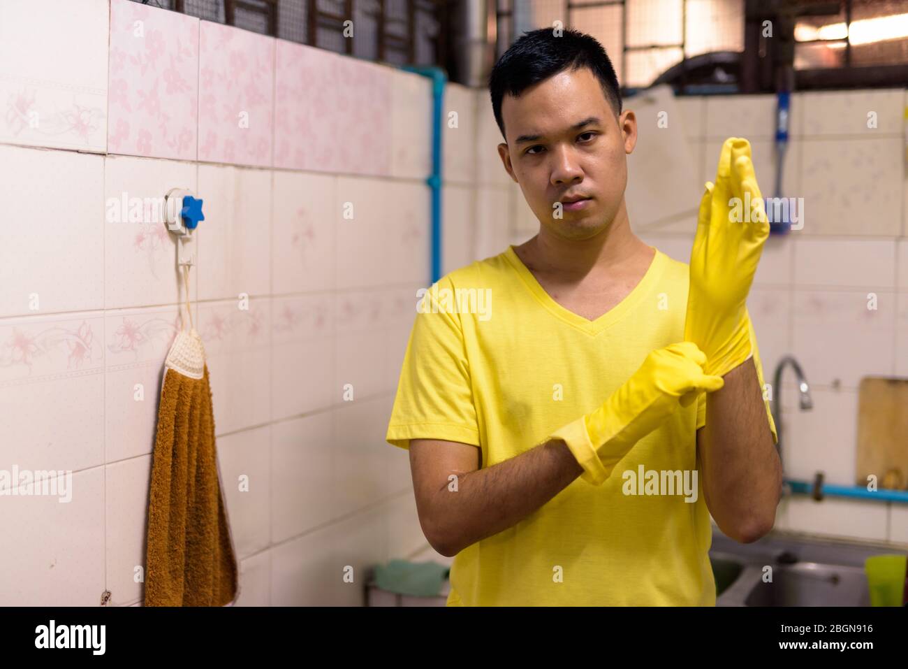 Portrait de jeune homme asiatique portant des gants lors de la pratique de tâches ménagères Banque D'Images