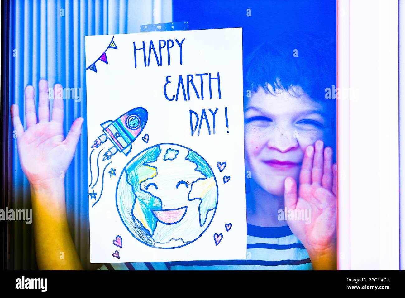 Droitwich, Worcestershire, Royaume-Uni. 22 avril 2020. Wera Khuit, 7 ans, apparaît à la fenêtre de sa maison à Droitwich Spa avec une affiche que sa mère a faite pour la Journée mondiale de la Terre. [Note: Autorisation parentale accordée] crédit: Peter Lopeman/Alay Live News Banque D'Images