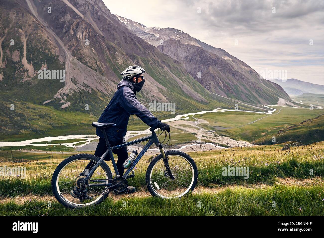 Man on mountain bike dans le casque, la vallée avec rivière à ciel nuageux fond. Banque D'Images