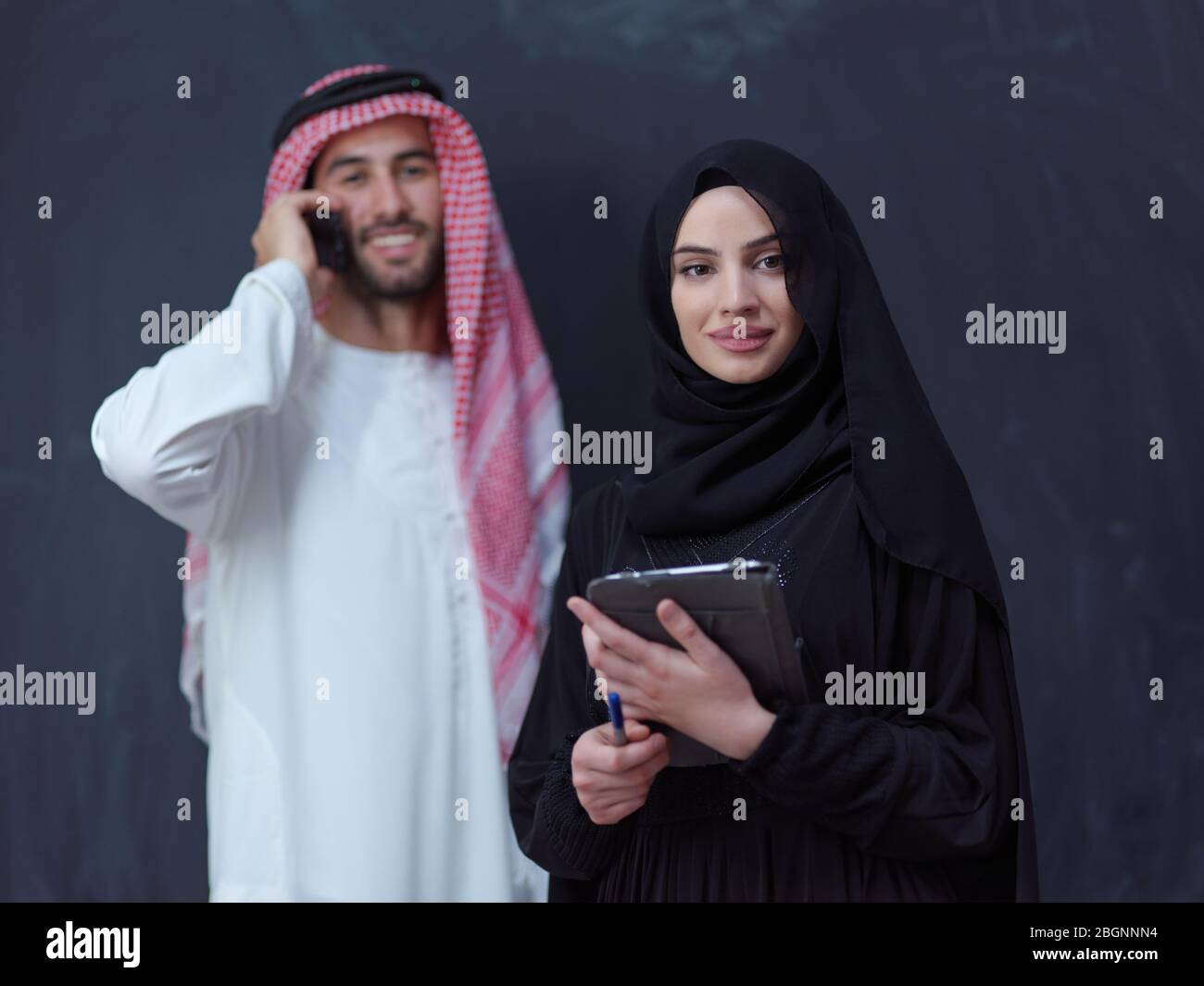 jeune homme d'affaires musulman arabe avec femme en robe hijab tendance utilisant téléphone mobile et tablette ordinateur devant un représentant noir de tableau de surveillance Banque D'Images