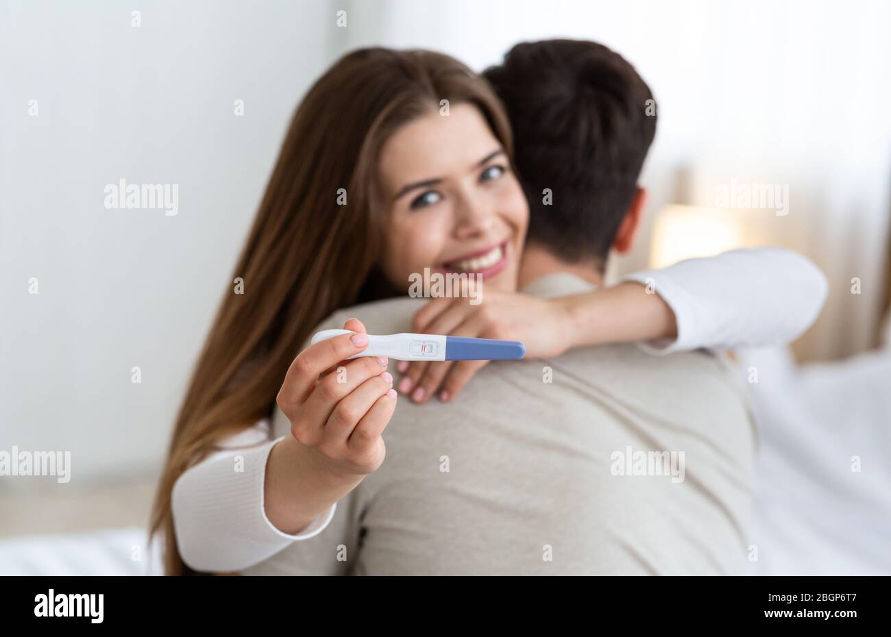 Se concentrer sur le test de grossesse. Jeune mari et femme embrassant Banque D'Images