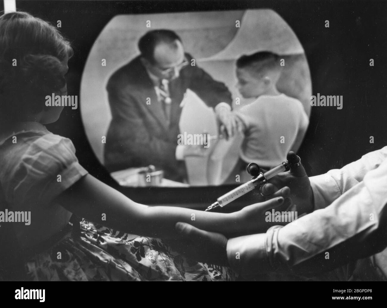 Une fille de huit ans recevant son propre vaccin contre la polio regarde le Dr Jonas Salk inoculer un garçon à la télévision en circuit fermé dans le cadre d'une formation télécast pour les médecins et les scientifiques, New York, NY, 4/12/1955. Banque D'Images