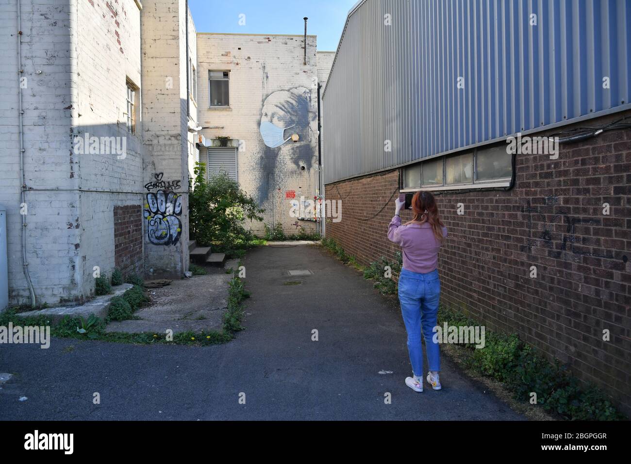 Une femme photographie la femme de Banksy's Girl avec une murale de tympan percé, qui a reçu un masque facial en signe de pandémie de coronavirus, à Hanovre place à Bristol, alors que le Royaume-Uni continue de se maintenir en position pour aider à freiner la propagation du coronavirus. Banque D'Images