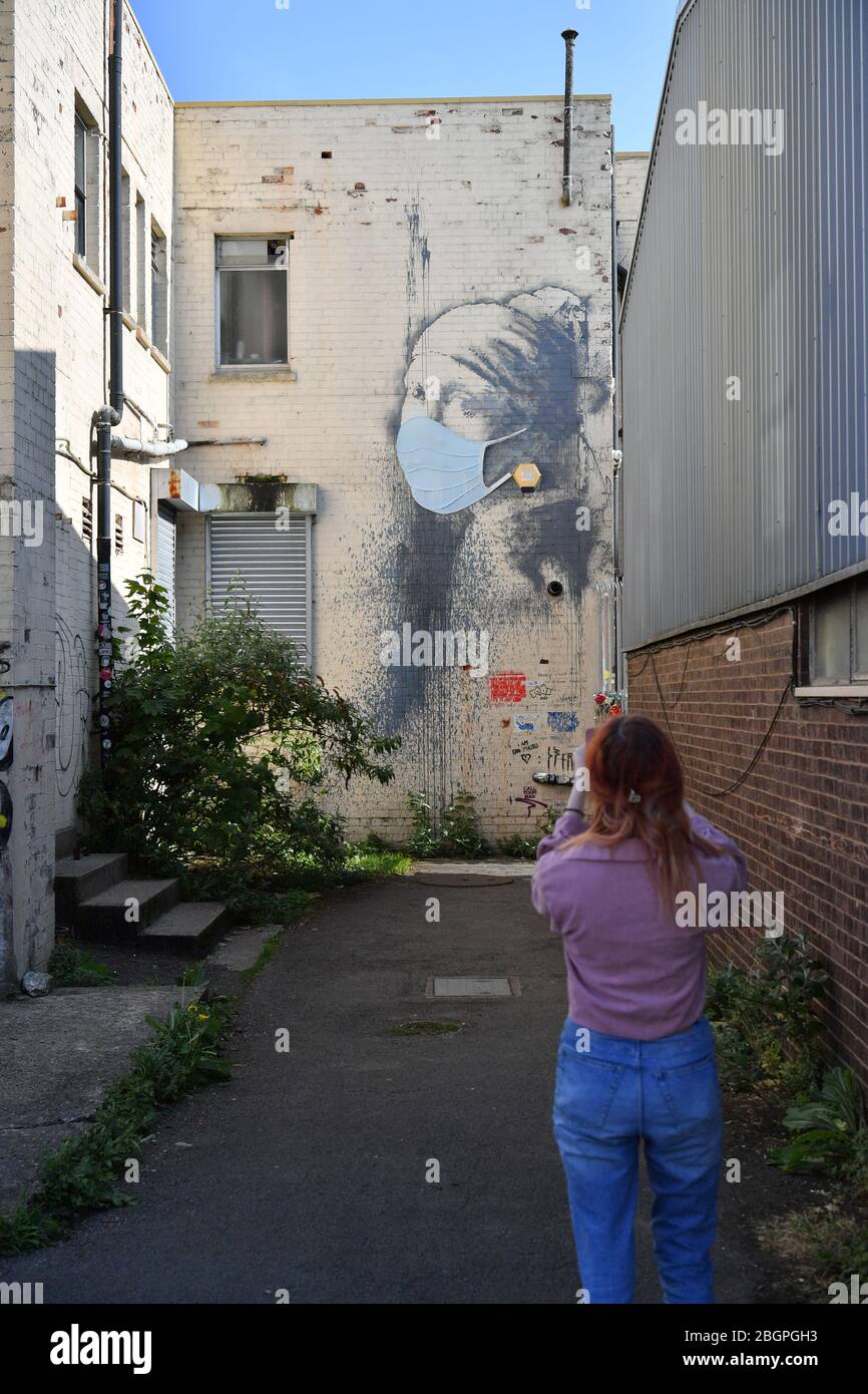 Une femme photographie la femme de Banksy's Girl avec une murale de tympan percé, qui a reçu un masque facial en signe de pandémie de coronavirus, à Hanovre place à Bristol, alors que le Royaume-Uni continue de se maintenir en position pour aider à freiner la propagation du coronavirus. Banque D'Images