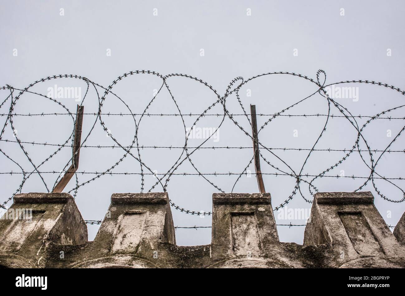 Fil concertina placé sur le dessus d'un mur. Ciel gris nuageux Banque D'Images