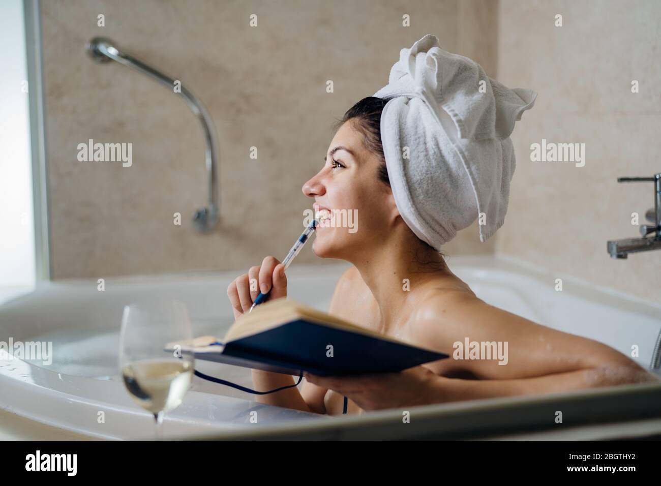 Une femme excitée qui aime se détendre dans le bain à la maison.Spa nuit d'auto-soin.personne créative inspirée écrivant gratitude agenda/journal.Liste de résolution.faire des plans Banque D'Images