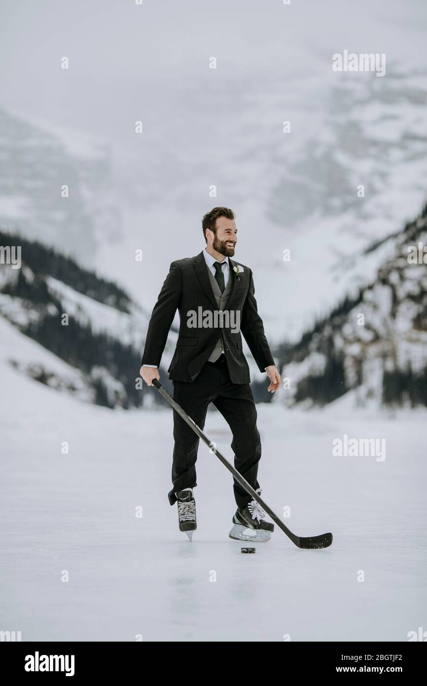 L'homme en costume noir, les patins de hockey et le bâton de hockey pose sur le lac gelé Banque D'Images