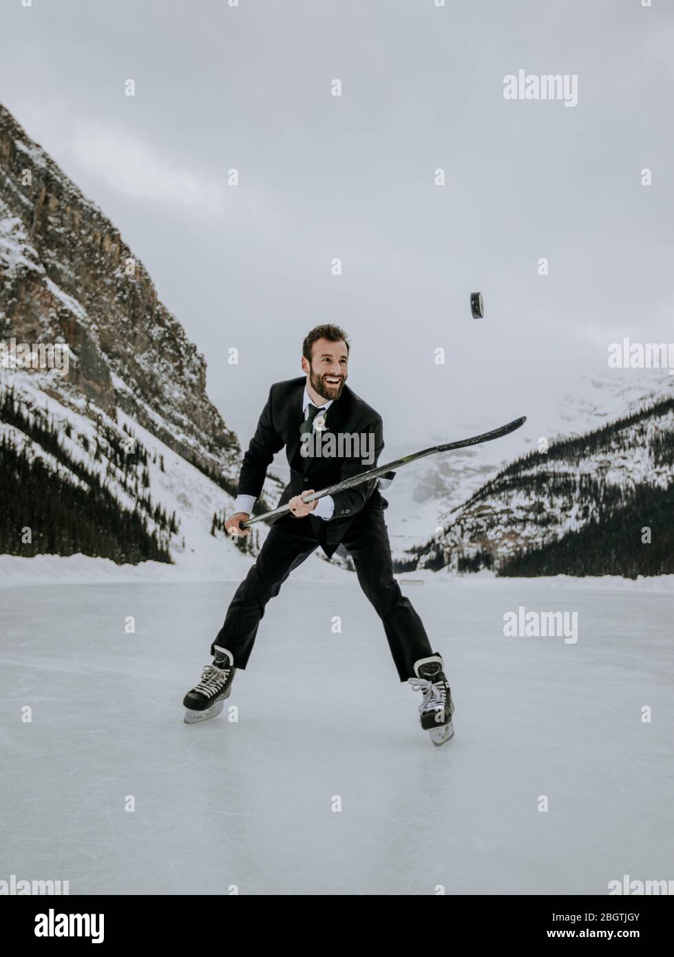 L'homme en costume et les patins à glace jongle avec le palet de hockey sur le lac Louise gelé Banque D'Images