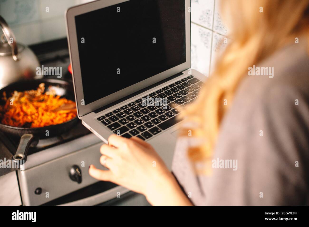 Jeune femme tenant un ordinateur portable pendant la cuisson de la nourriture dans la cuisine Banque D'Images