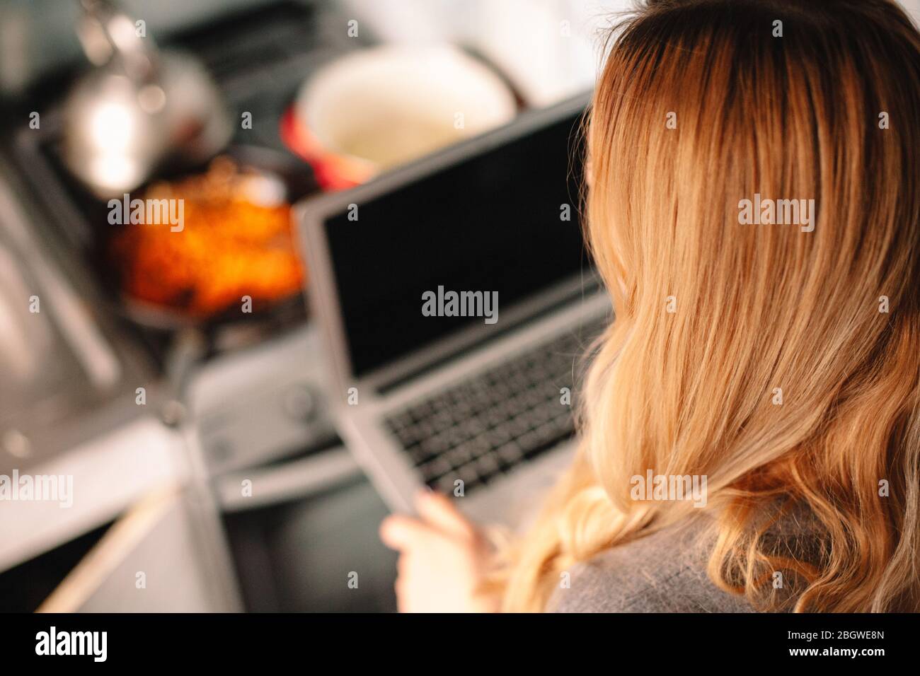 Jeune femme tenant un ordinateur portable pendant la cuisson de la nourriture dans la cuisine Banque D'Images