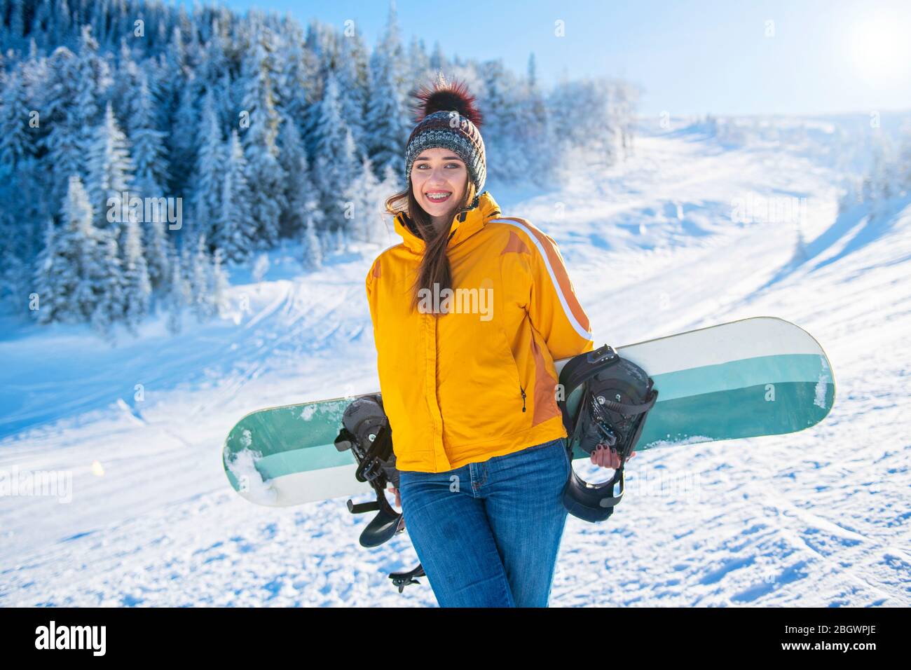 La sportive féminine tient le snowboard en montagne dans un Jean Banque D'Images