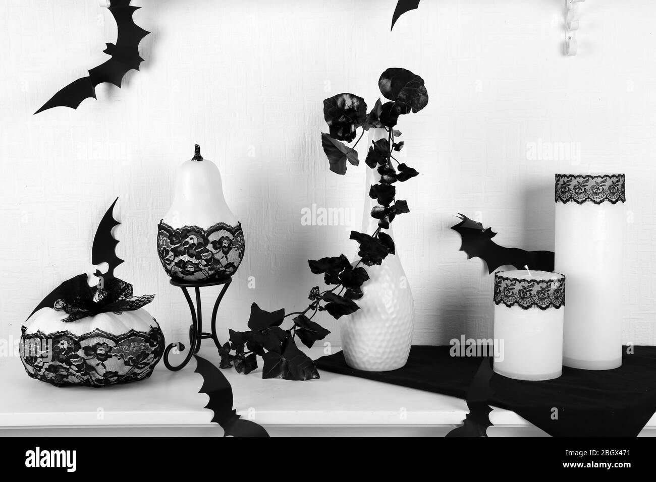Bougies avec dentelle noire et citrouilles blanches sur la table sur fond de mur blanc Banque D'Images