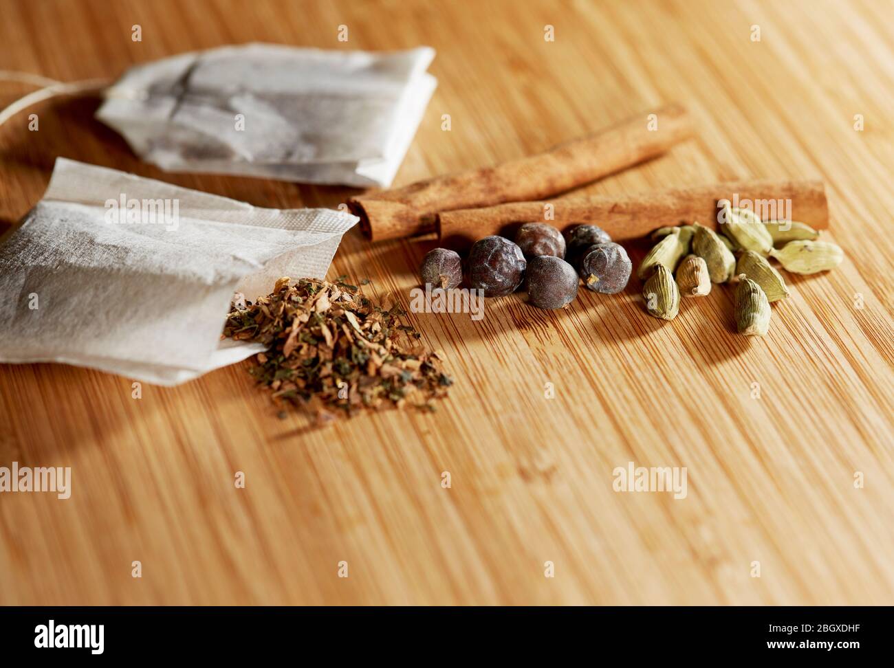 Gros plan sur un sac de thé ouvert à base de plantes avec des herbes libres et des baies de genévrier et des bâtons de cannelle sur un plateau de découpe en bambou avec peu de profondeur de champ Banque D'Images