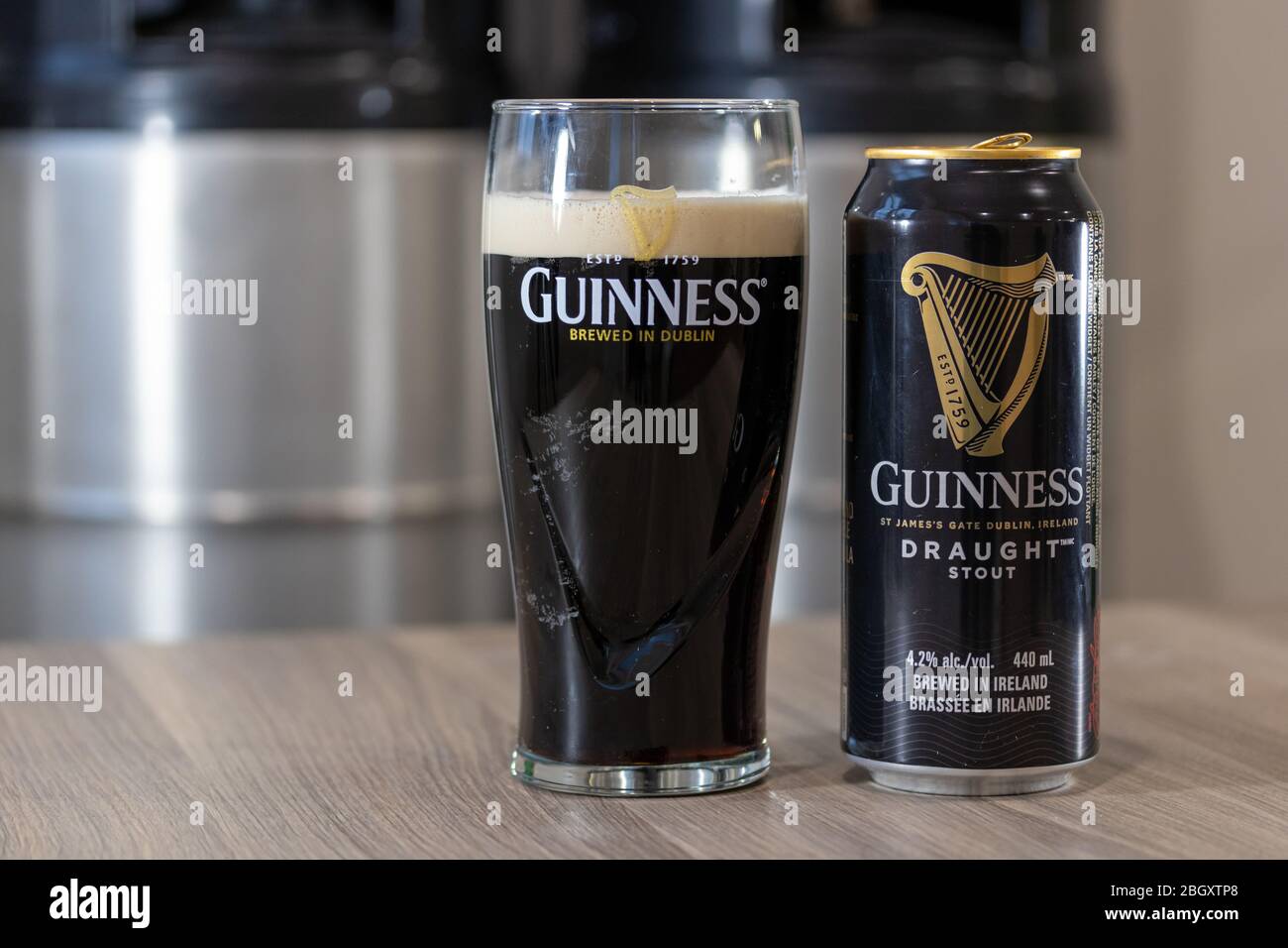 La bière Guinness draft Shout peut sur une table à côté d'un verre de bière dans un verre Guinness avec des kegs empilés en arrière-plan. Banque D'Images