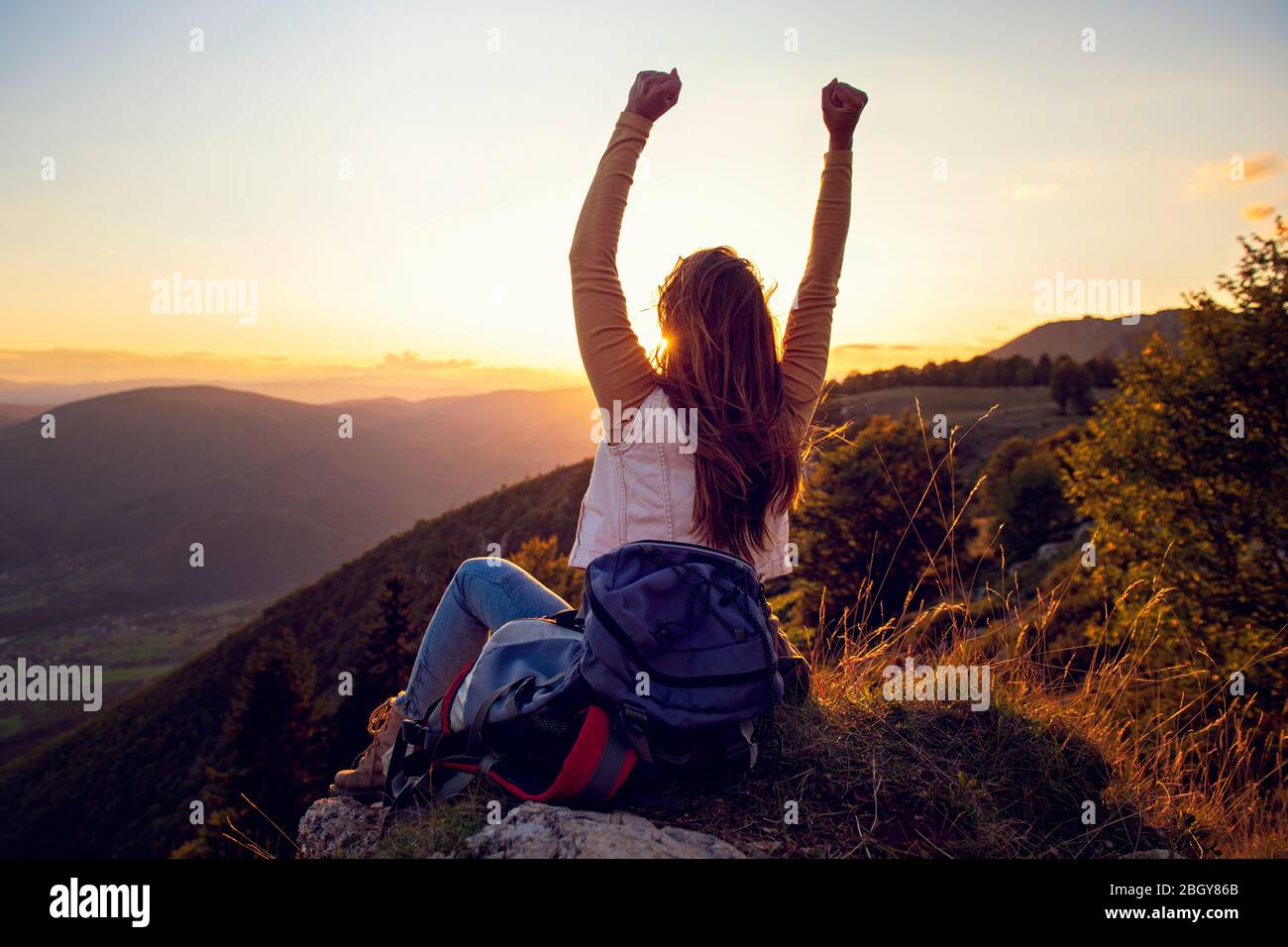 La jeune femme monte à la main sur le sommet de la montagne et coucher du soleil ciel fond abstrait. Banque D'Images