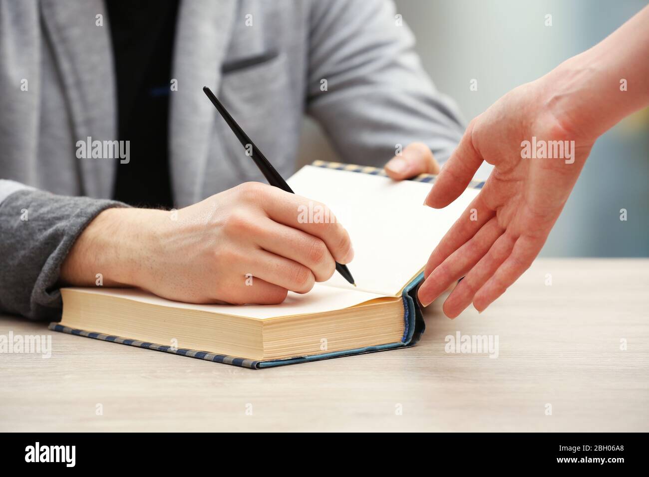 Auteur signe autographe dans son propre livre à une table en bois sur fond flou léger Banque D'Images