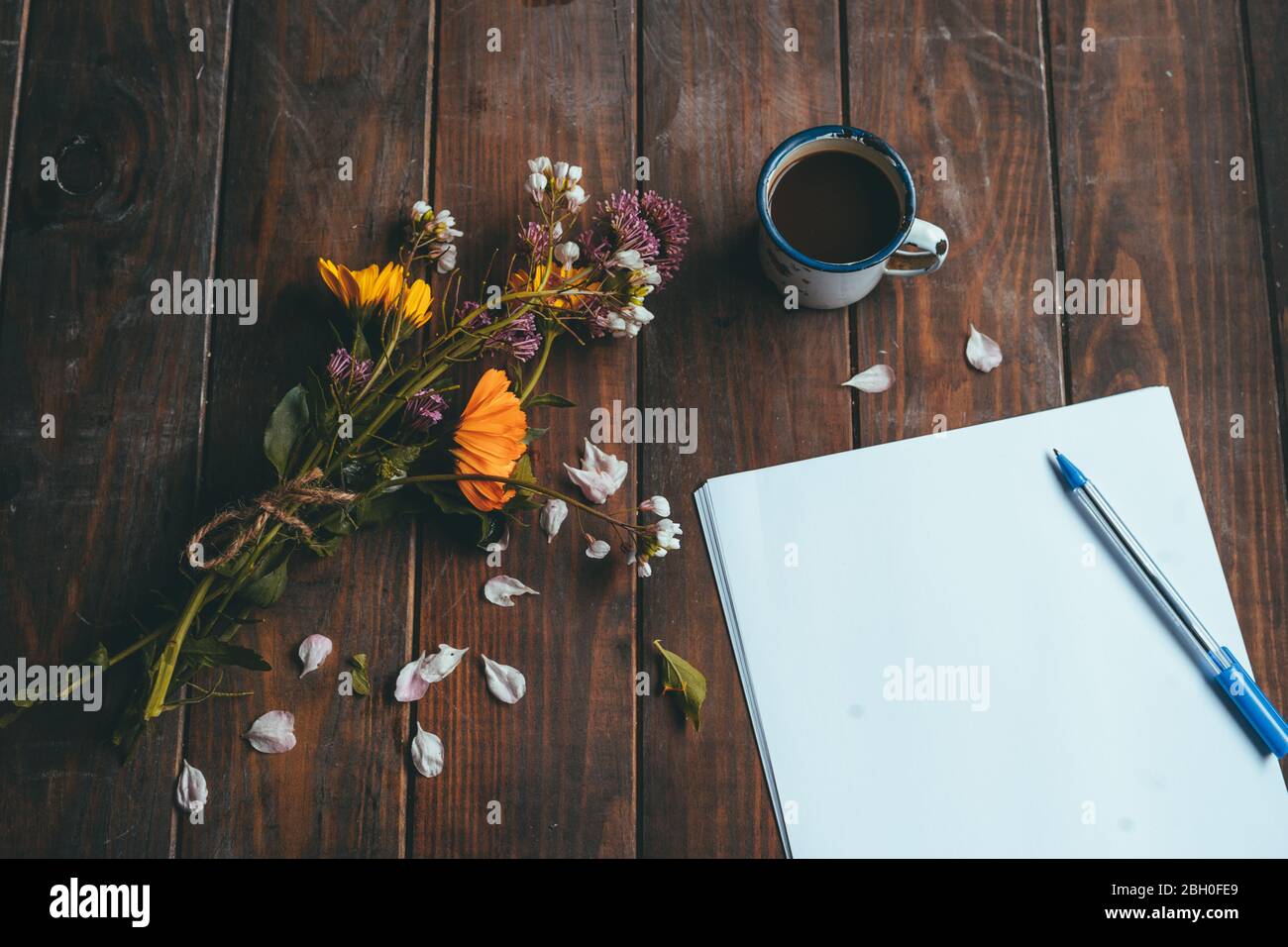 Papier vierge et stylo à fleurs printanières avec une petite tasse de café blanc sur une table rustique en bois Banque D'Images