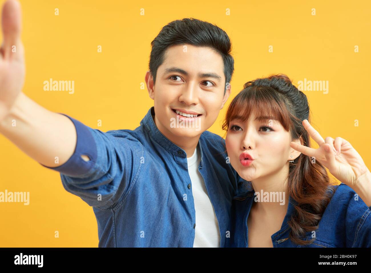 Portrait de heureux homme et femme souriant et posant sur l'appareil photo isolé sur fond jaune Banque D'Images