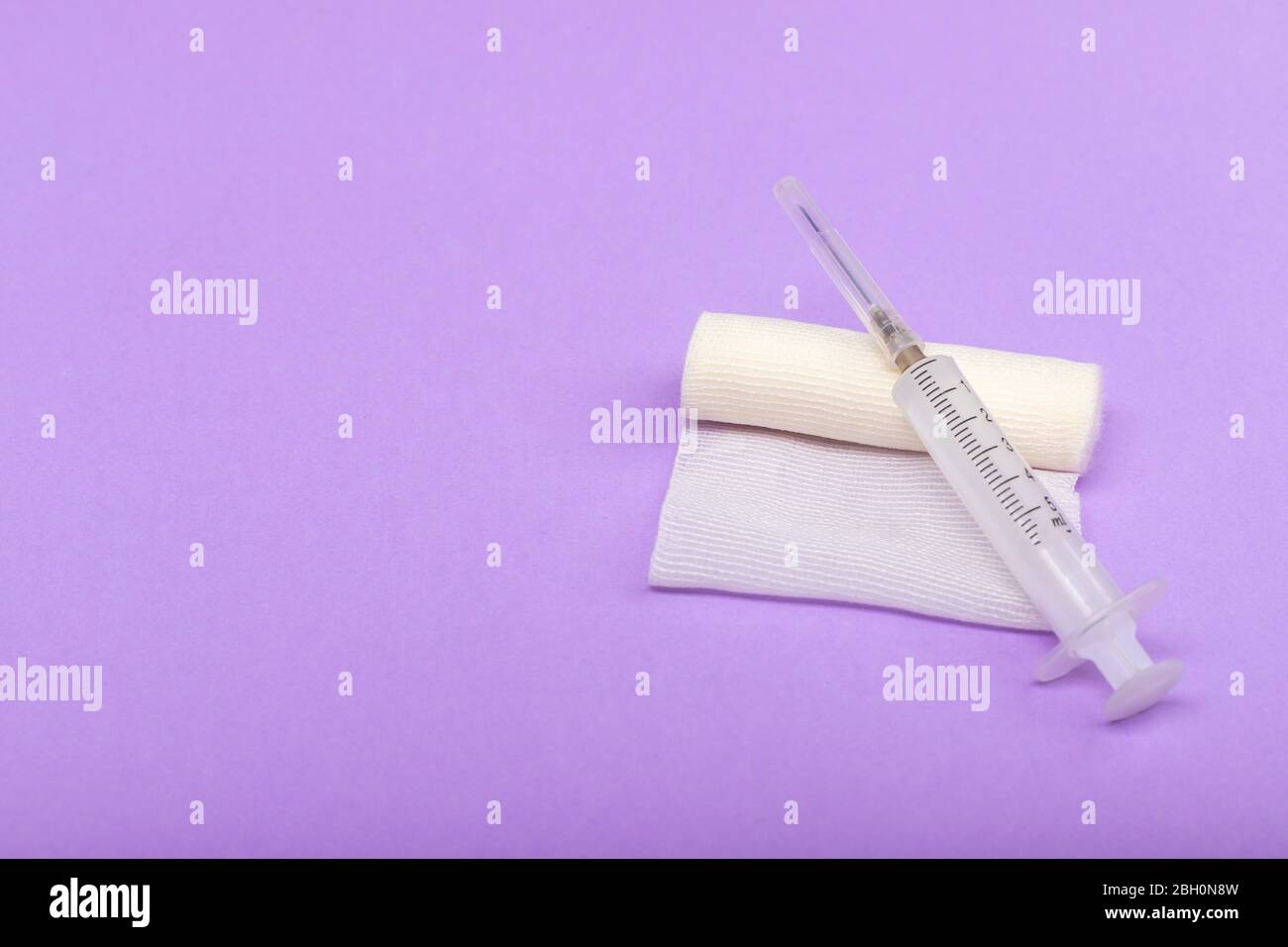 Bandage médical et seringue sur fond lilas. Un rouleau de gaze sur lequel repose la seringue. Pansement à usage médical. Espace pour le texte sur la gauche Banque D'Images