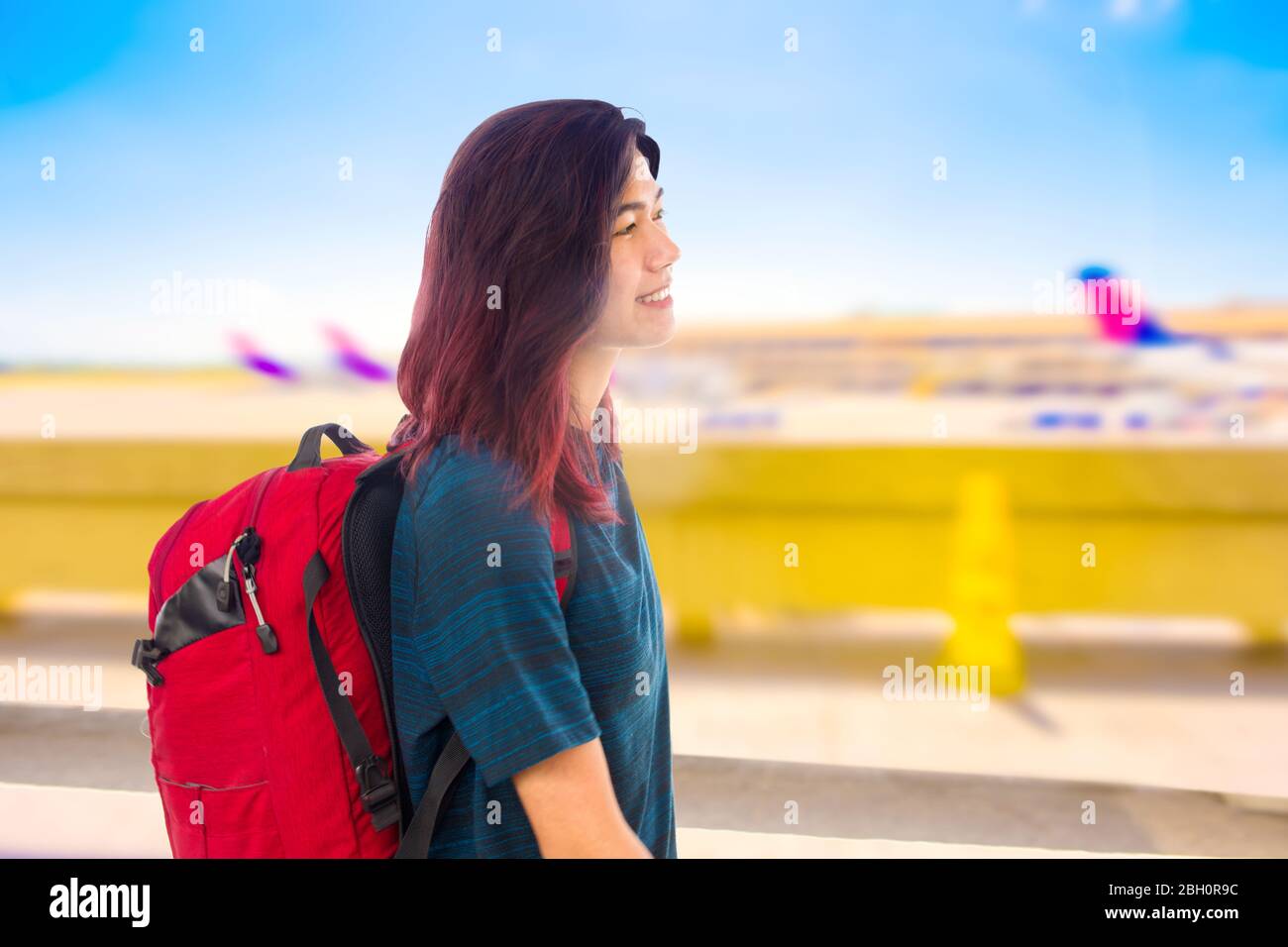 Une fille asiatique souriante avec sac à dos rouge qui passe devant des rangées d'avions garés à l'aéroport le jour ensoleillé Banque D'Images