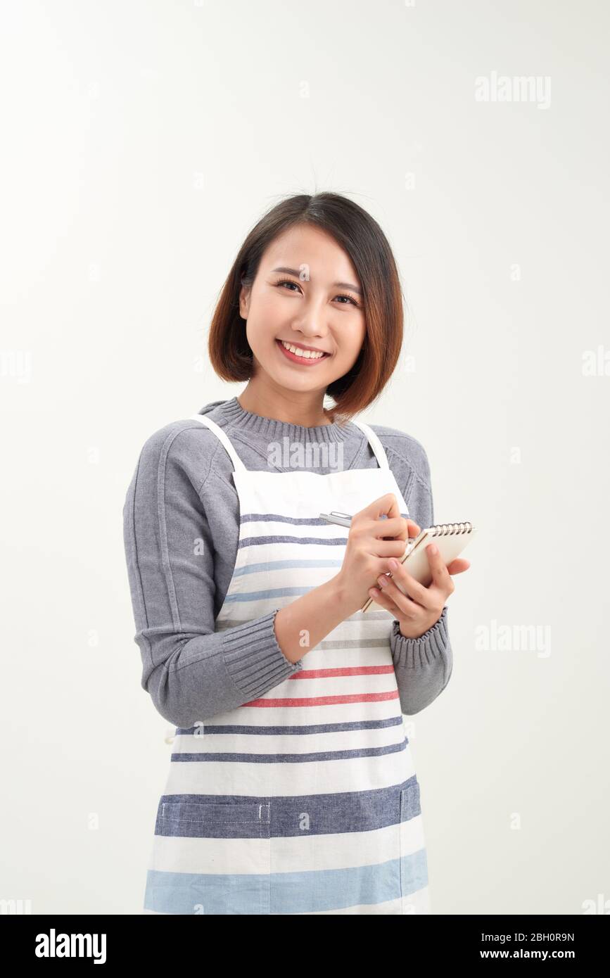 Bonne fille asiatique serveur en tablier écrire la commande et regarder l'appareil photo Banque D'Images