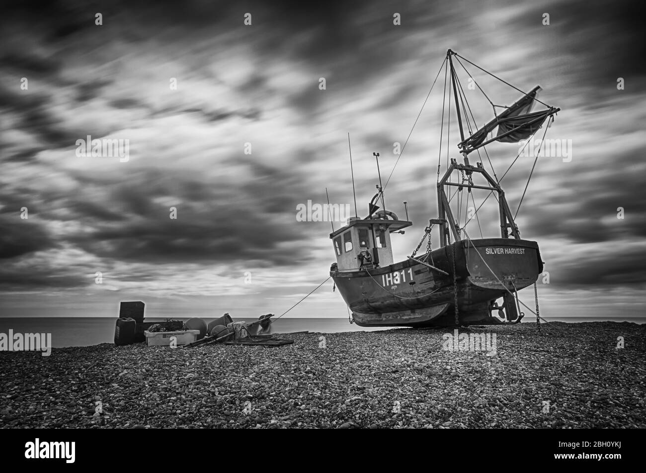 Une photo d'exposition longue d'un bateau de pêche rustique reposant sur une plage de galets à Aldborough, sur la côte du Suffolk Banque D'Images