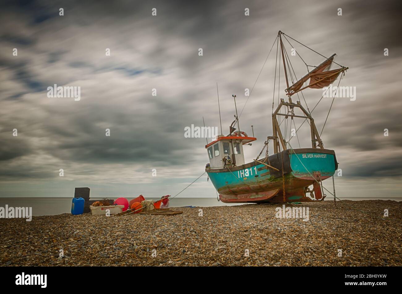 Une photo d'exposition longue d'un bateau de pêche rustique reposant sur une plage de galets à Aldborough, sur la côte du Suffolk Banque D'Images