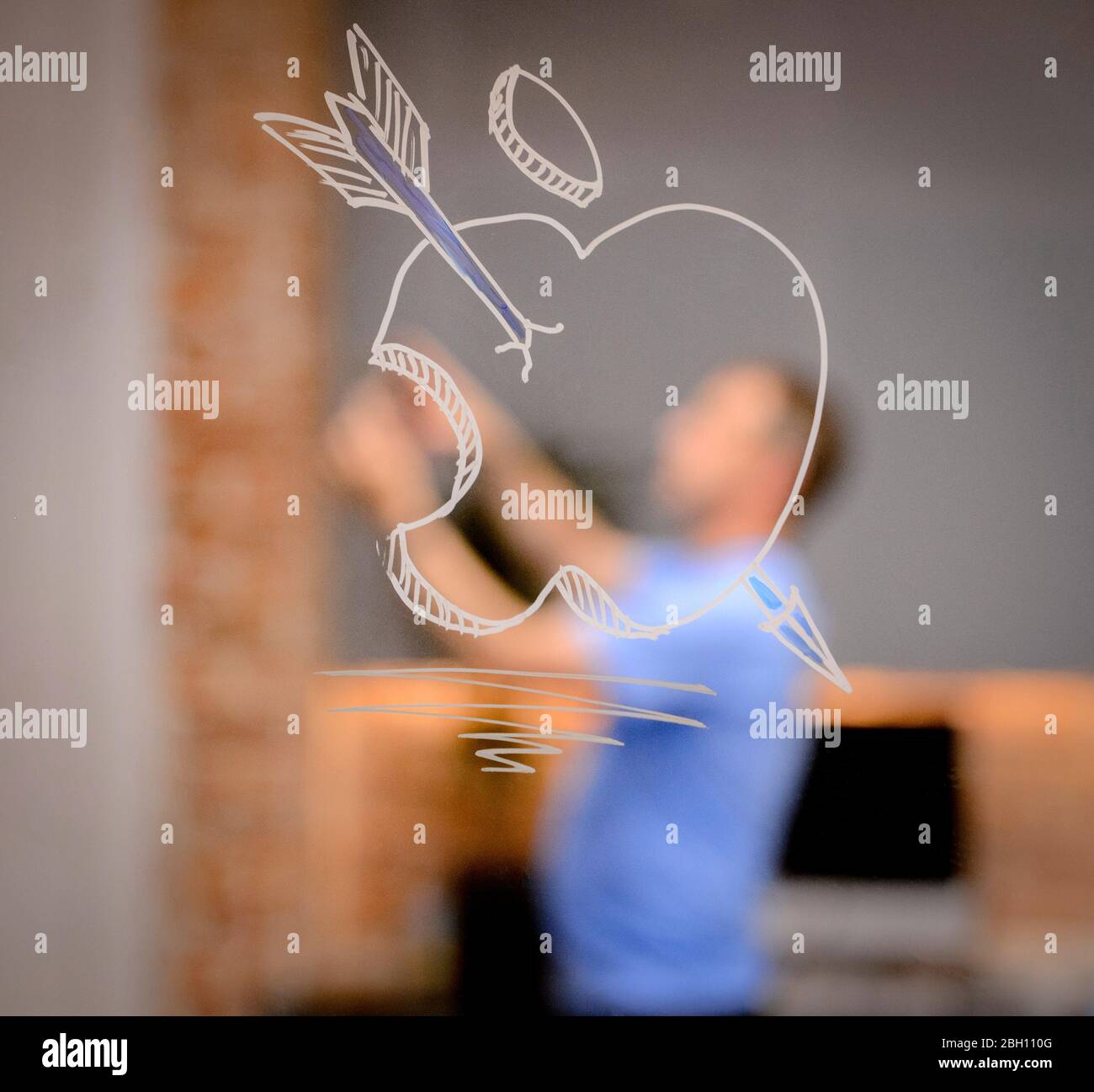 Une pomme avec une flèche dessinée à travers elle peinte sur une fenêtre. À distance, un homme utilise un iPad ou un téléphone pour prendre une photo. Banque D'Images